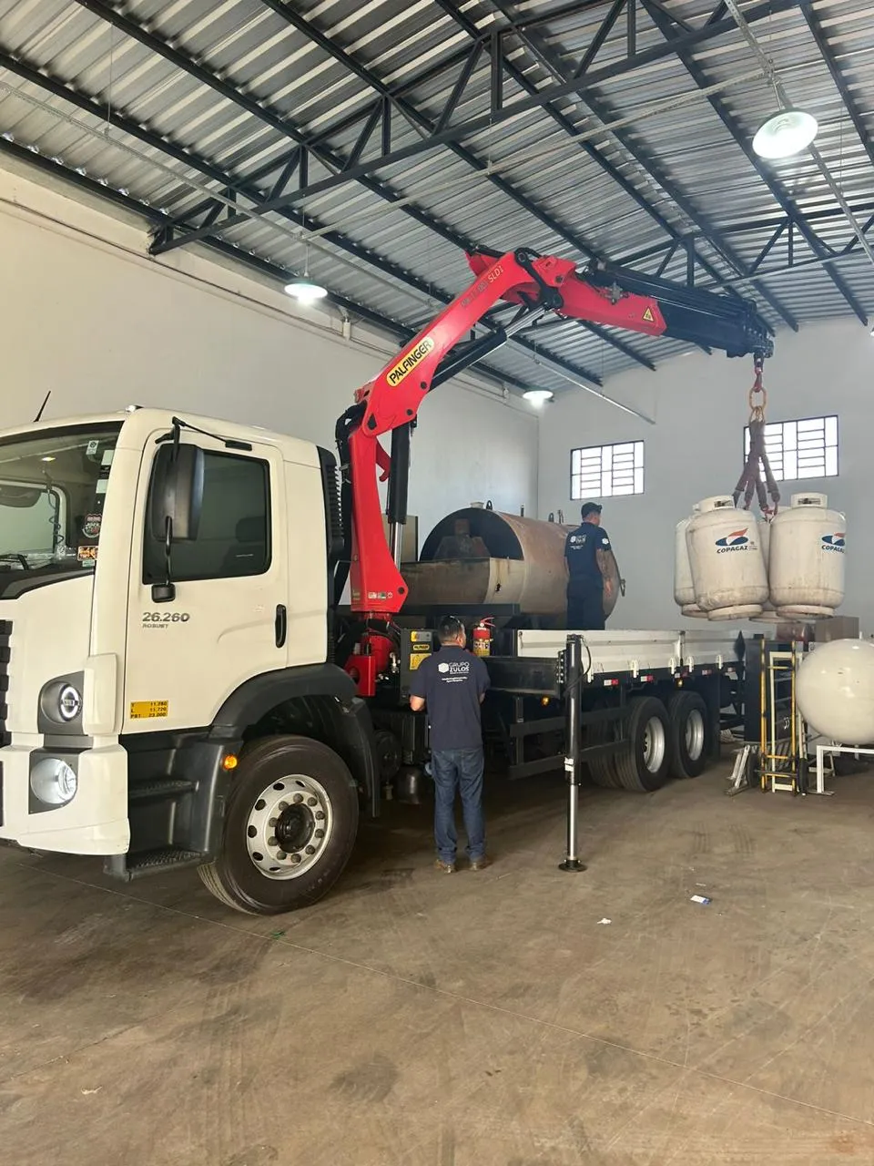 Caminhão da Frota Zulos carregando tanque de gás grande dentro de armazém industrial